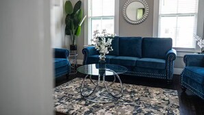 A living room with a blue sofa, a glass coffee table, and a patterned rug. - Petersburg Vacation Gem 3BR - Private Backyard (Petersburg)