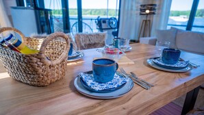 Een eettafel met blauwe keramische kopjes, een mand met flessen en uitzicht op de omgeving.