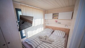 Een slaapkamer met een bed, een wandtelevisie, een plank met spullen, en een raam met gordijnen.