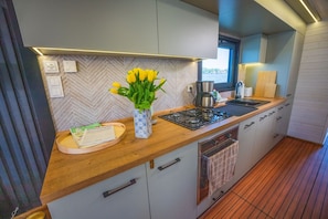 Une cuisine moderne avec un revêtement mural en motif chevrons, un plan de travail en bois, une cuisinière à gaz et une fenêtre donnant sur un plan d’eau.