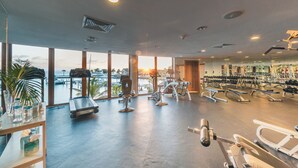 Ein Fitnessstudio mit unterschiedlichen Trainingsgeräten, großen Fenstern und Blick auf den Ozean.