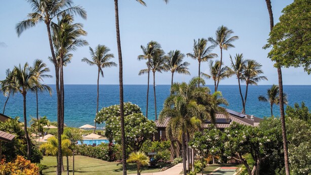 A tropical resort with palm trees, a pool, and a view of the ocean. - Ground-Floor Gem in Wailea Ekahi Village (Kihei)