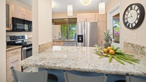 A modern kitchen with granite countertops, stainless steel appliances, and a central island with chairs. - Ground-Floor Gem in Wailea Ekahi Village (Kihei)