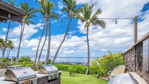 An outdoor grill area with stone walls, a view of the ocean, and palm trees. - Ground-Floor Gem in Wailea Ekahi Village (Kihei)