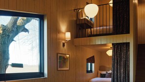 Una habitación acogedora con un gran ventanal, un sofá verde, una mesita con libros y una escalera a un nivel superior.