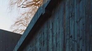 Una pared de madera rústica con un letrero de metal, dos plantas en macetas y una rueda decorativa.