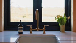 Una cocina con un lavamanos, dos ventanas y vistas a un paisaje arenoso.