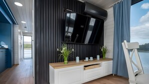 A modern living room with a large TV mounted on a dark wall, a white console table with plants, and a view of the outdoors.