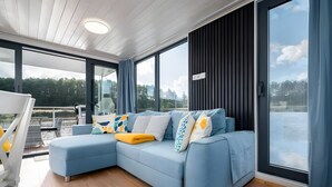 A modern living room with a blue sectional sofa, a glass door leading to a balcony, and a view of a body of water.
