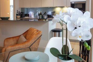 Una cocina moderna con una isla central, un comedor con mesa de vidrio y una planta de orquídea blanca.
