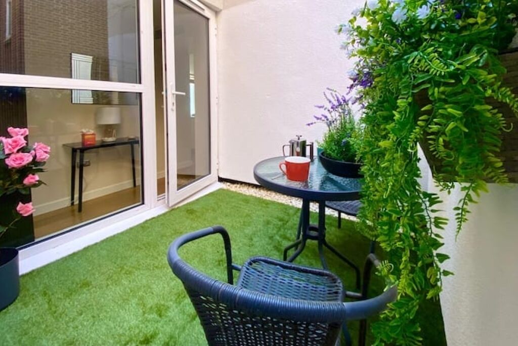 A small patio with artificial grass, a table, chairs, and a potted plant.