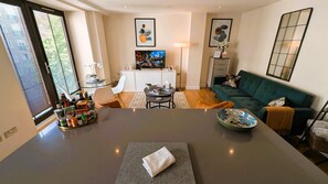 Ein modernes Wohnzimmer mit einem dunkelgrauen Tisch, einem grünen Sofa und einem Essbereich mit einem Glastisch und Stühlen.