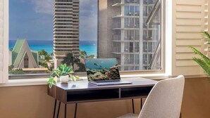 A desk with a laptop, a potted plant, and a view of tall buildings and a beach. - Chic Suite W/ Direct Ocean Views & Free Parking (Honolulu)