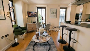Una sala de estar moderna con un sofá verde, una mesa de centro con revistas y una cocina con mostrador y taburetes.