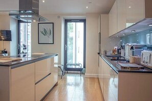 A modern kitchen with a central island, a dining area, and a view of the outdoors. - Elegant Westminster Retreat: Stylish 2-Bed, 2-Bath with Air-Con (London)