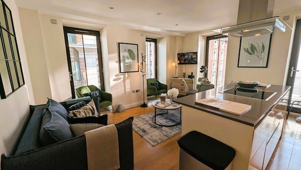 Una sala de estar moderna con un sofá, una mesa de centro y una zona de cocina con mostrador y lavamanos.