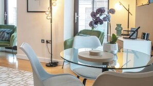 Una sala de estar moderna con una mesa de centro de vidrio, sillas de color claro, un sofá verde y una lámpara de pie.