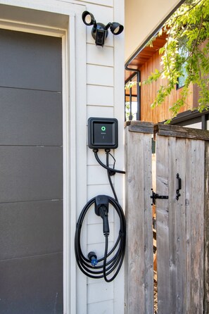 An electric vehicle charging station mounted on a house wall with a wooden fence nearby. - Luxe 6BR Oasis | Pool•Hot Tub•Games | Near DTown (Austin)