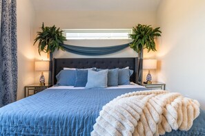 A bedroom with a large bed, two nightstands, a window with draped curtains, and two potted plants. - Luxe 6BR Oasis | Pool•Hot Tub•Games | Near DTown (Austin)