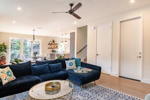 A modern living room with a dark blue sectional sofa, a glass coffee table, and a patterned rug. - Luxe 6BR Oasis | Pool•Hot Tub•Games | Near DTown (Austin)