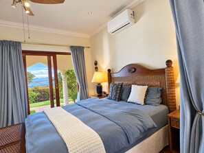 Une chambre d’hôtel comprenant un lit, une table de chevet, une lampe, un appareil de climatisation et une vue sur l’extérieur.