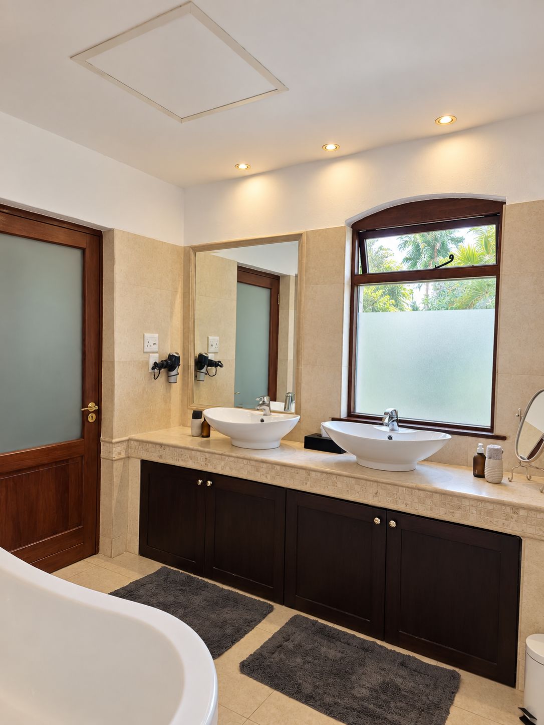 A modern bathroom with two sinks, a large mirror, and a bathtub.