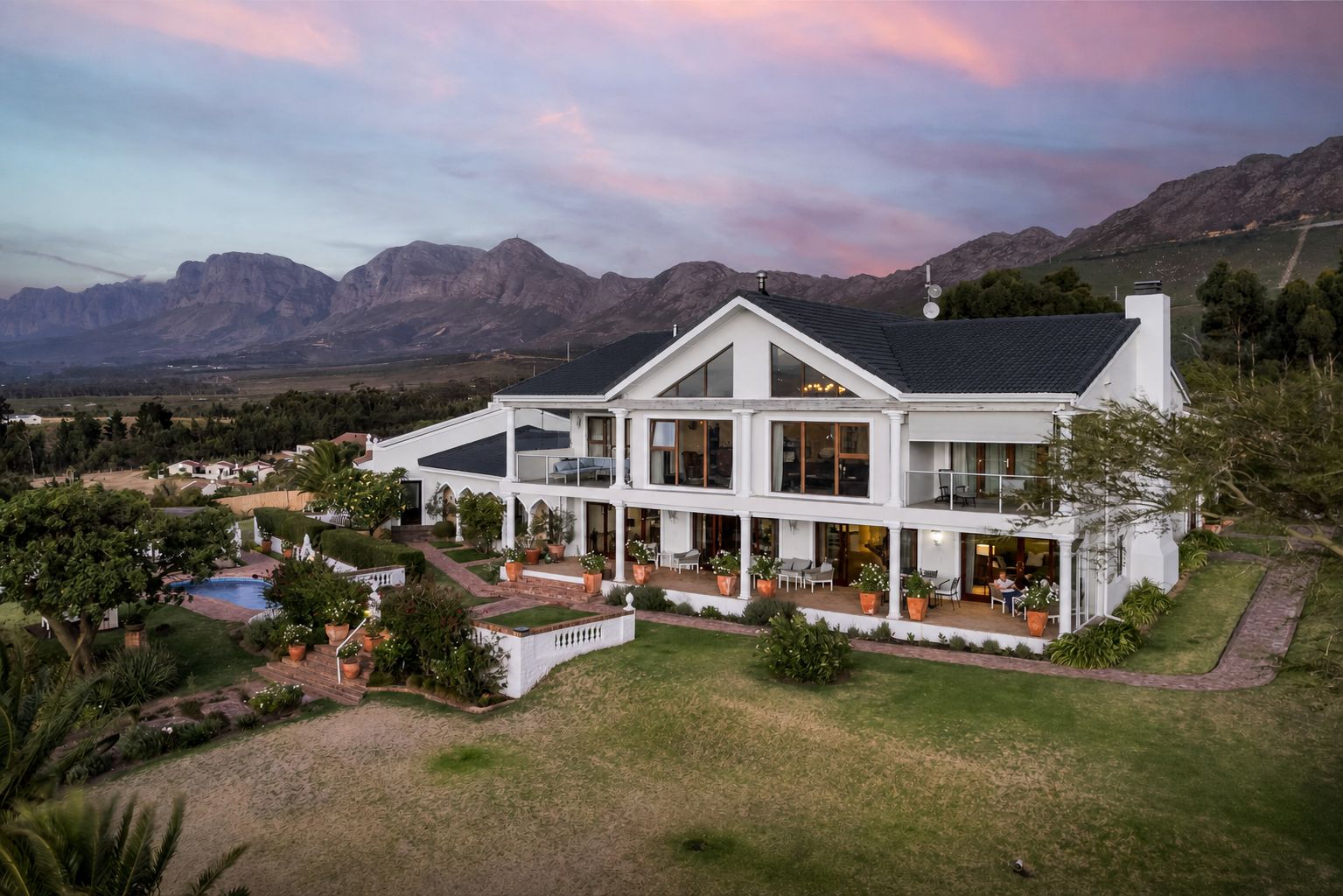 A large two-story house with a spacious patio area, surrounded by a well-maintained lawn and a swimming pool.