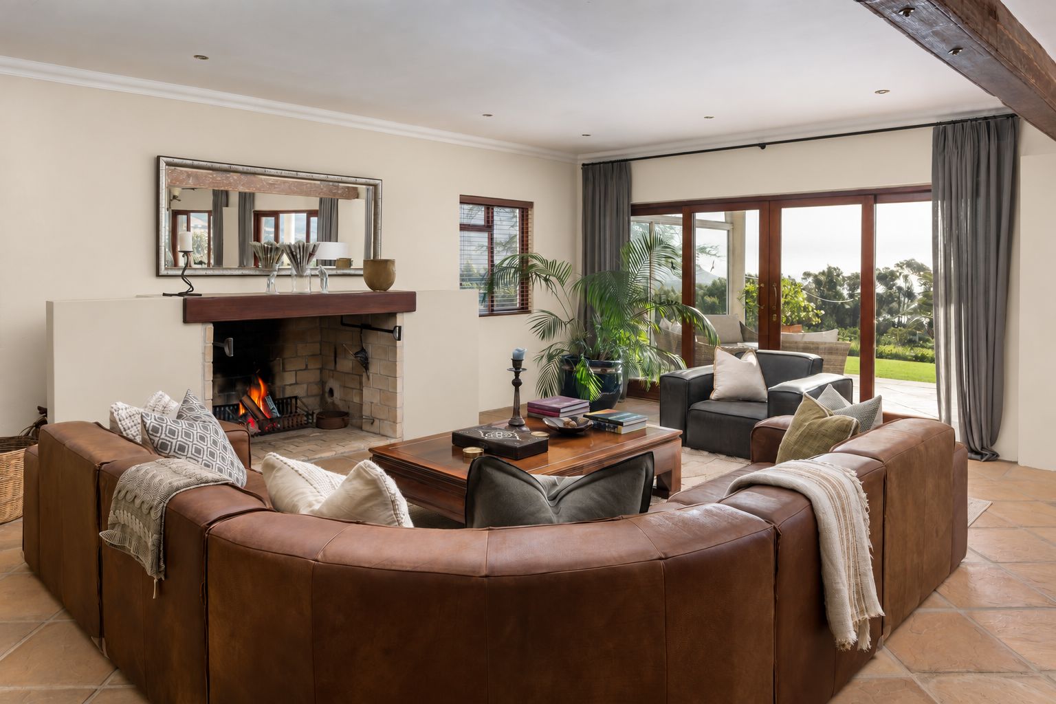 A living room with a fireplace, a large mirror, a sofa, a coffee table, and a view through large windows.