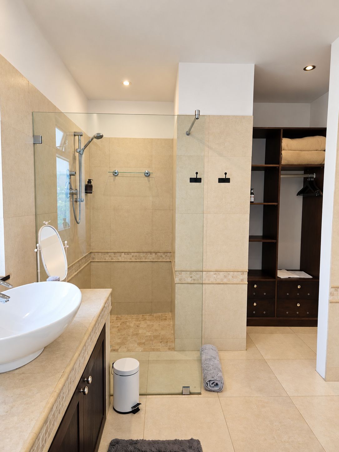 A modern bathroom with a large sink, mirror, shower, and walk-in closet.