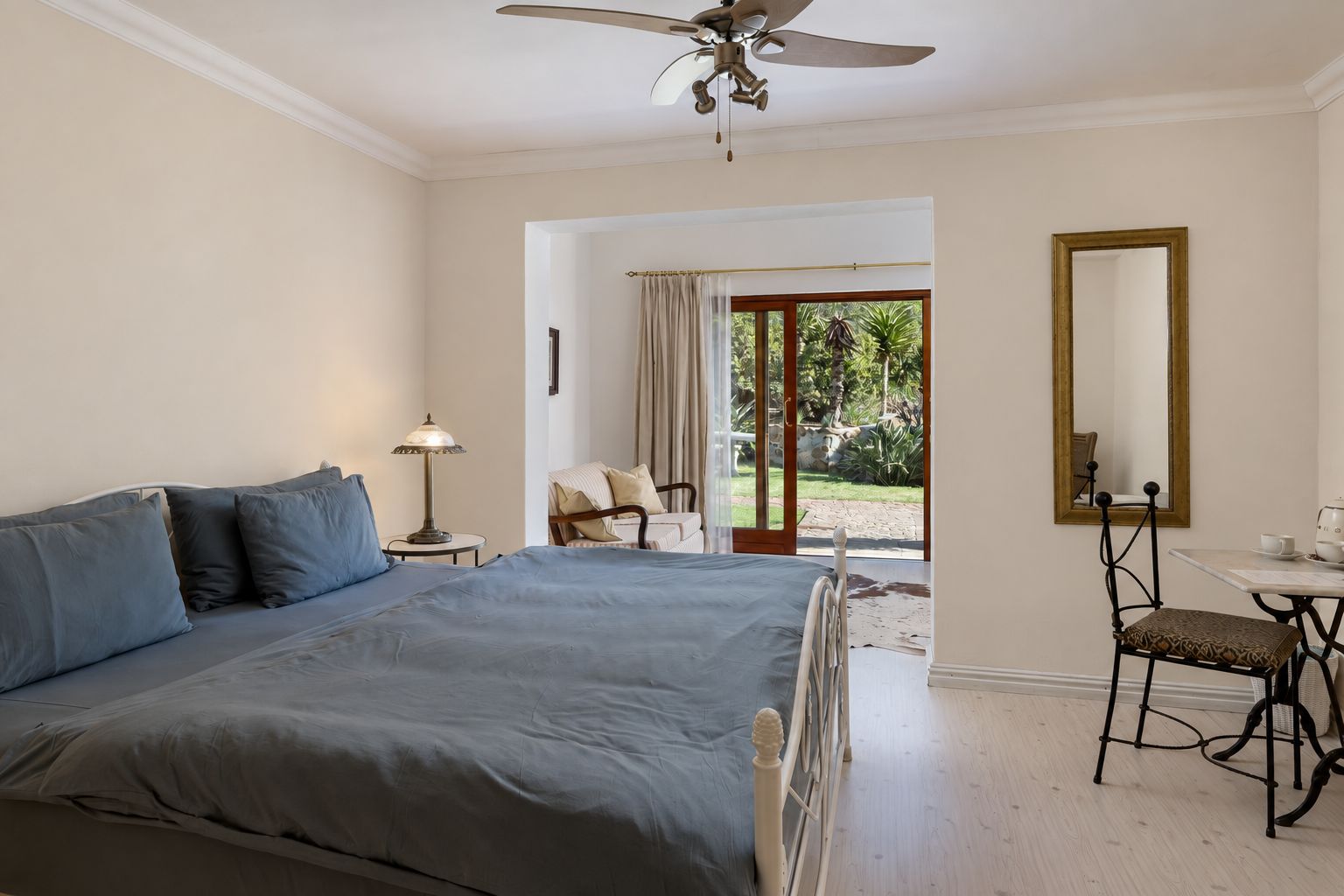 A bedroom with a large bed, a desk, a chair, a ceiling fan, and a view of the outdoors.