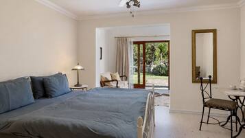 A bedroom with a large bed, a desk, a chair, a ceiling fan, and a view of the outdoors.