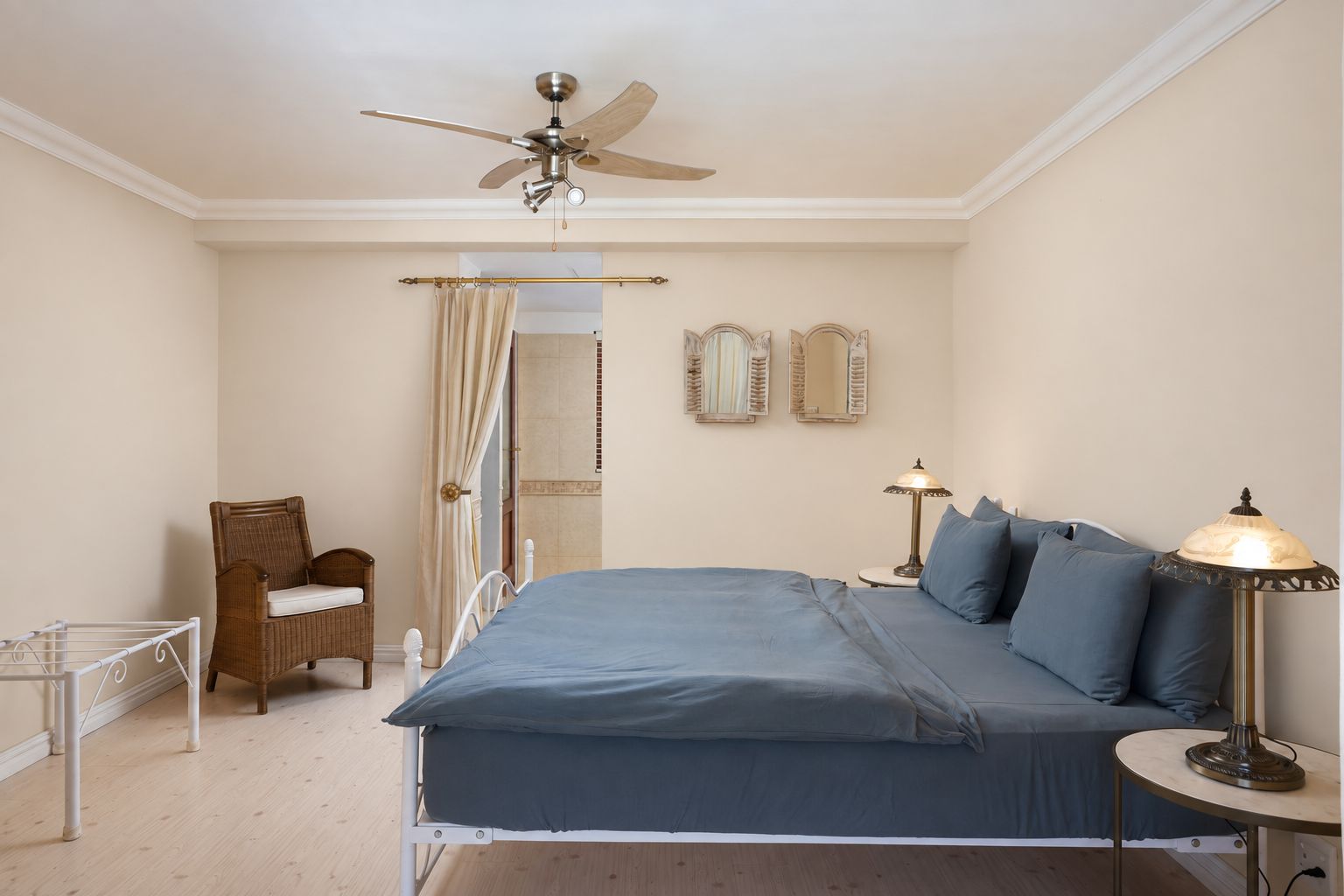 Une chambre à coucher comprenant un lit, un ventilateur de plafond, une chaise, une table de chevet avec une lampe et deux miroirs muraux.