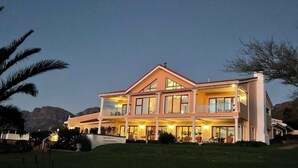 Un'ampia casa a due piani con numerosi balconi e ampie finestre, circondata da un prato curato e palme.