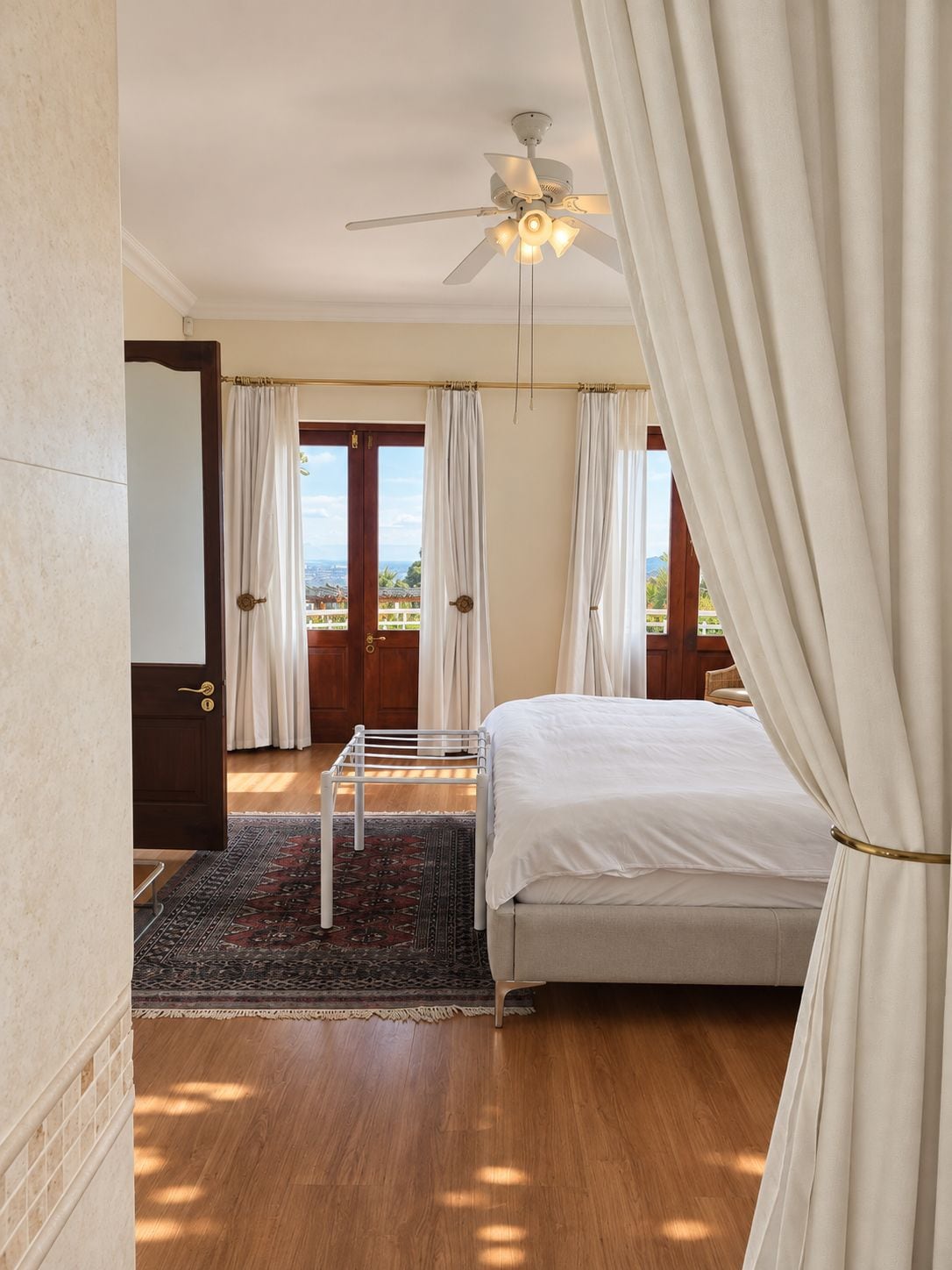 A bedroom with a bed, a ceiling fan, a view through a door, and a rug.