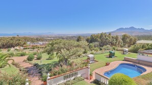 Un jardin aménagé avec une piscine, un espace barbecue et une vue sur les montagnes lointaines.