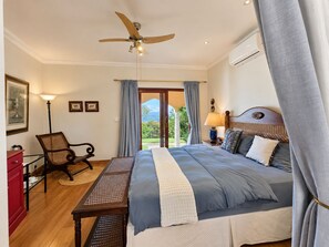 A bedroom with a bed, a desk, a chair, a ceiling fan, and a view of the outdoors. - Apricot Gardens Boutique Guesthouse (Cape Town)