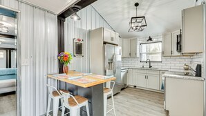 Una cocina moderna con armarios blancos, un refrigerador de acero inoxidable y una mesa de comedor de madera con taburetes de bar.