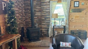 Ein gemütliches Blockhaus-Interieur mit Steinwand, Kamin, Weihnachtsstamm, Ledersessel und Holztisch.