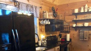 Eine kleine Küche mit Holzausstattung, einem schwarzen Kühlschrank, einer Kaffeemaschine und einem gemusterten Teppich.