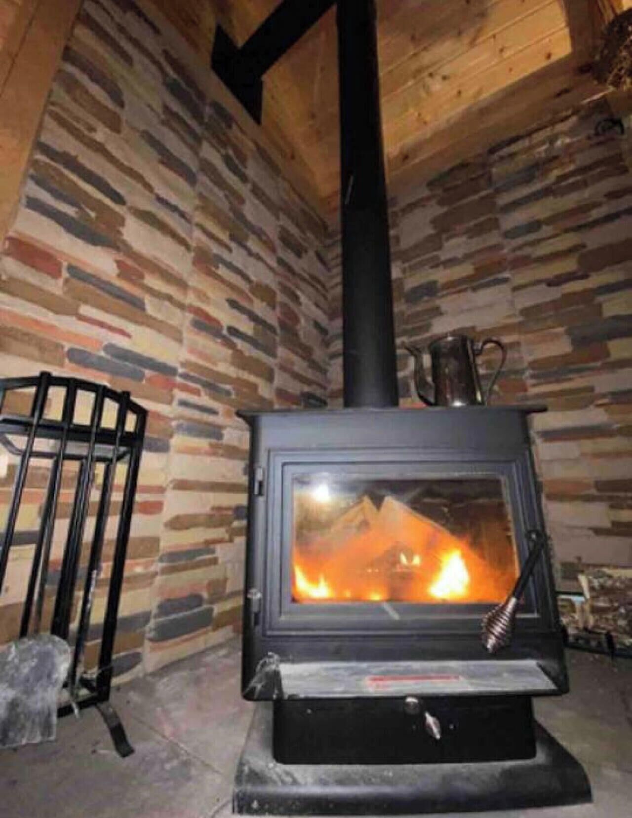 Una estufa de leña en una habitación con pared de piedra y un banco de metal.