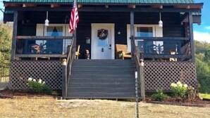 Eine zweistöckige Blockhütte mit einem grünen Metalldach, einer Veranda mit Geländer und einer amerikanischen Flagge.