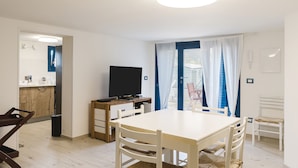 Une pièce moderne comprenant une table à manger, des chaises, un téléviseur et un coin cuisine.