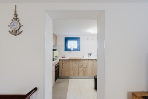 Una cocina con armarios de madera, una ventana con marco azul y un reloj fijado a la pared.