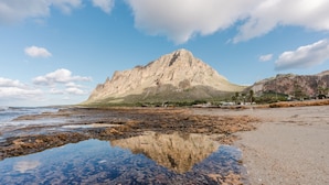 Une montagne avec une plage rocheuse au premier plan et un ciel dégagé.