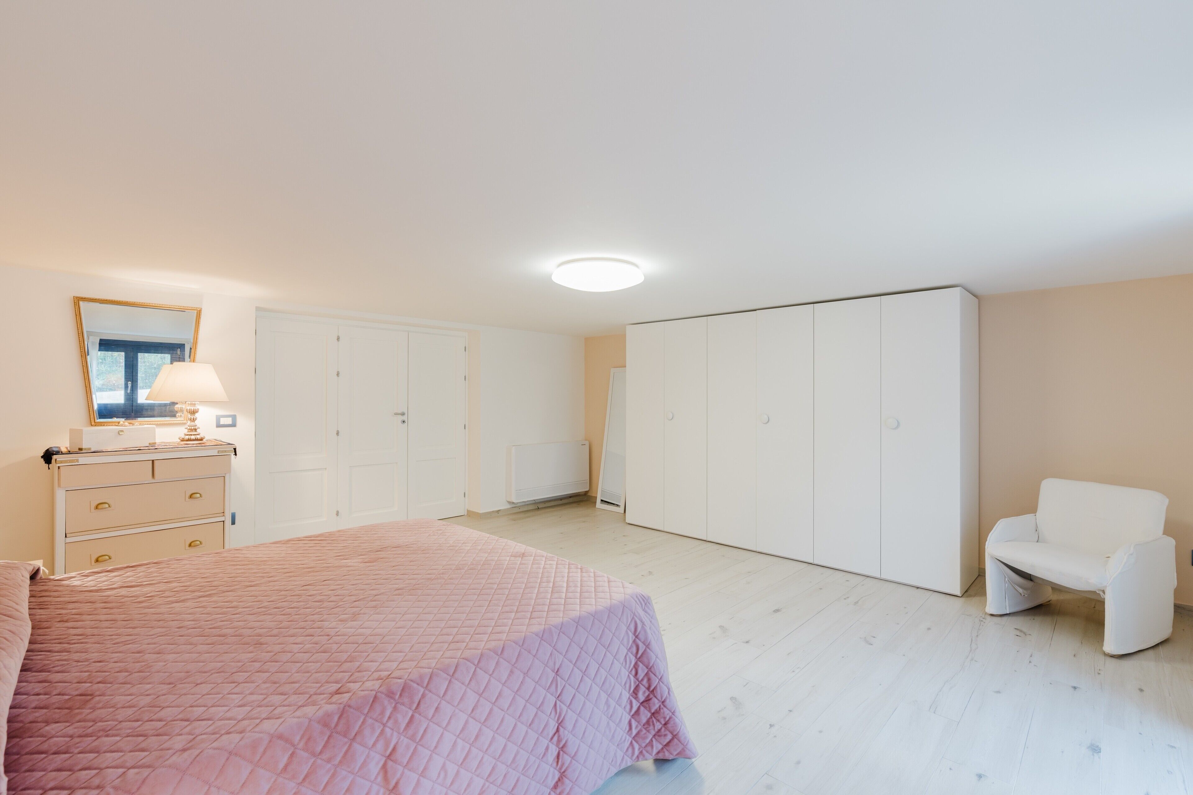 A bedroom with a bed, dresser, mirror, wardrobe, and a chair.