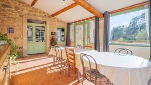 Comedor con mesa, sillas, paredes de piedra, vigas de madera y vista a través de una ventana.