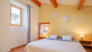 Un dormitorio con cama, dos mesitas de noche, una ventana con cortinas y un adorno en la pared.