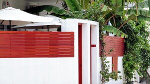 Un edificio moderno con fachada blanca y detalles en rojo, que presenta una planta grande y macetas con plantas en la entrada.