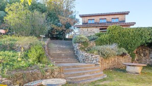 Una escalera de piedra conduce a un edificio de madera con tejado de baldosas, rodeado de vegetación y muros de piedra.