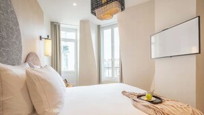 Una camera d'hotel con un letto grande, una TV a schermo piatto, una finestra con tende e un lampadario decorativo.
